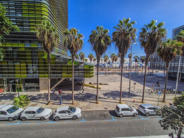A modern building with a curved facade and a parking area with several cars and palm trees.