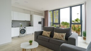 Eine moderne Wohnung mit grauem Sofa, einem kleinen runden Tisch, einer Waschmaschine und einer Küchenzeile.