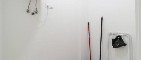 Canto de um quarto com parede branca, luminária, esfregão, vassoura e balde.