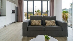 Ein modernes Wohnzimmer mit einer grauen Couch, einem kleinen weißen Tisch und einem großen Fenster mit Vorhängen.