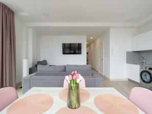 Una sala moderna con un sofá gris, una mesa de comedor con individuales rosas y un florero con flores.