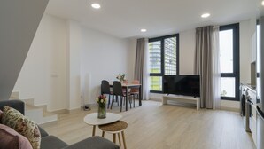 Una sala de estar moderna con un sofá, una mesa de comedor con sillas, un televisor y una zona de cocina con horno.