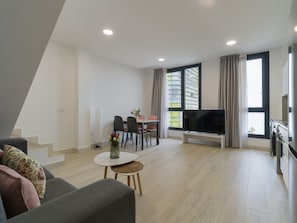 A modern living room with a sofa, a dining table with chairs, a TV, and a kitchen area with an oven.
