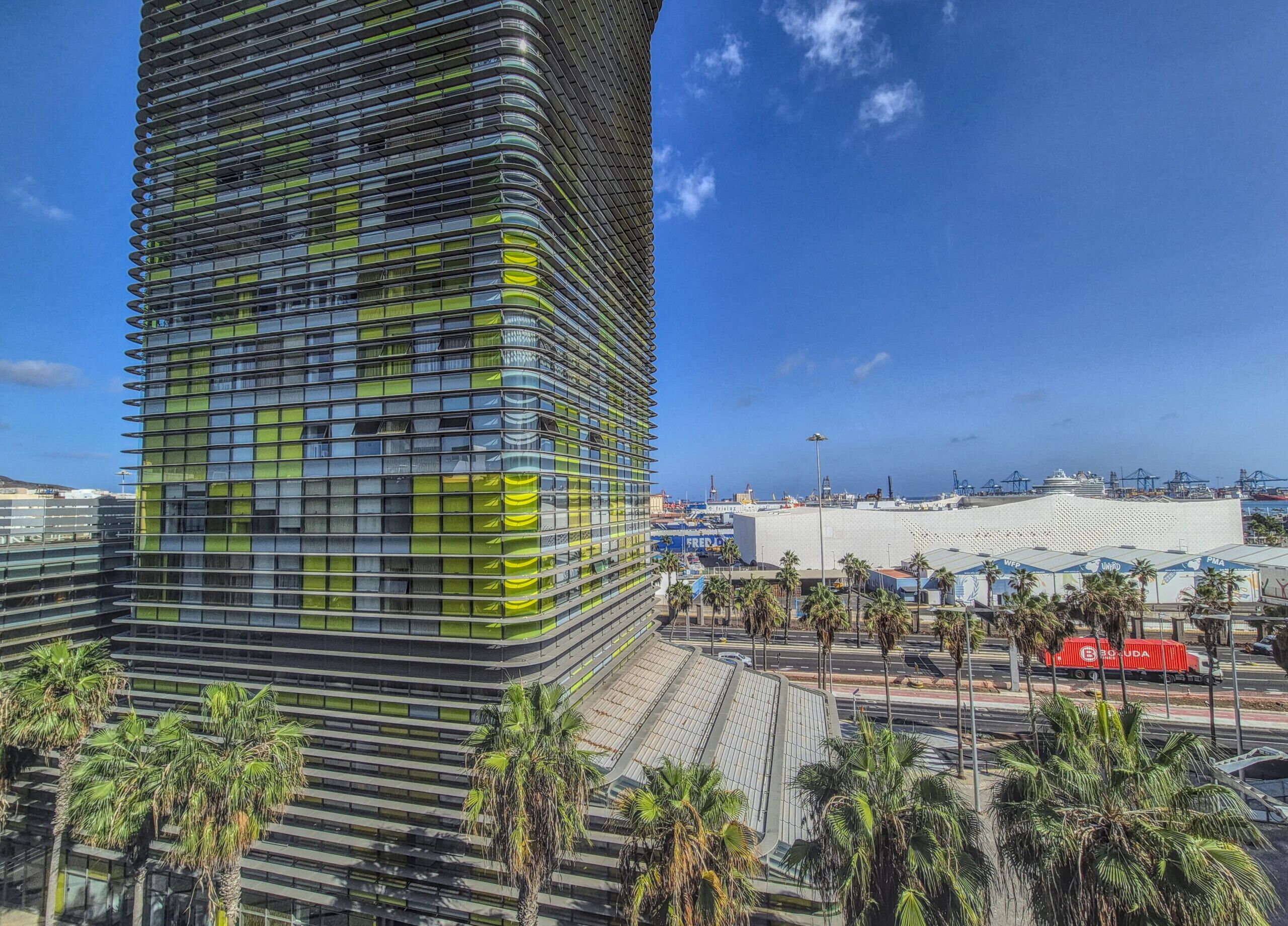 A modern building with a curved facade, surrounded by palm trees and a clear blue sky.