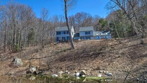 A two-story house with a large window and a chimney, surrounded by trees and a small pond. - Home on 40 Acres with Pinball in Game Room (Manchester)