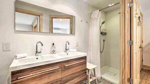 A modern bathroom with a wooden vanity, a large mirror, two sinks, and a glass-enclosed shower. - Home on 40 Acres with Pinball in Game Room (Manchester)