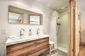 A modern bathroom with a wooden vanity, a large mirror, two sinks, and a glass-enclosed shower.