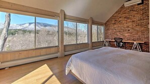 Ein Schlafzimmer mit einem großen Bett, einem Schreibtisch und einem Stuhl, mit Ziegelwand und großen Fenstern.