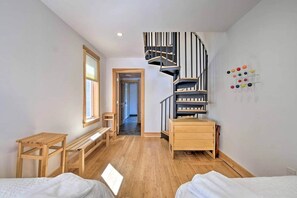 A bedroom with a wooden bed, a small wooden desk, a bench, a spiral staircase, and a wall-mounted color palette.