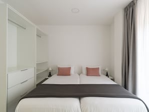 Une chambre avec deux lits, une armoire, des lampes de chevet et une fenêtre avec des rideaux.