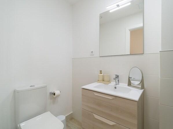 A modern bathroom with a toilet, sink, mirror, and storage cabinet.