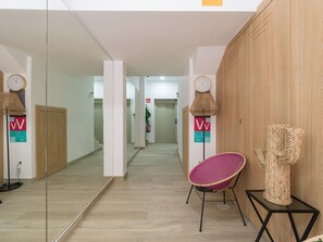 Un couloir avec un miroir, une chaise en osier, une horloge et un mur en bois.