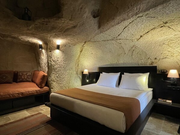 A bedroom with a stone ceiling, a bed with white linens, a brown sofa, and two bedside lamps. - Casa Cappadocia (Ürgüp)