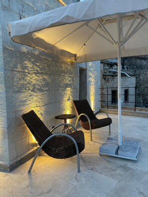 A covered outdoor seating area with wicker chairs and a small table, set against a textured wall with stone elements. - Casa Cappadocia (Ürgüp)