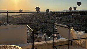 A terrace with a view of hot air balloons, a woven table, and lounge chairs. - Casa Cappadocia (Ürgüp)