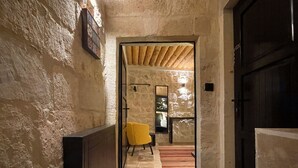 A narrow hallway with textured walls, a yellow chair, and a wooden door. - Casa Cappadocia (Ürgüp)