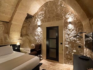 A bedroom with a stone wall, a bed, a chair, a desk, and a door. - Casa Cappadocia (Ürgüp)