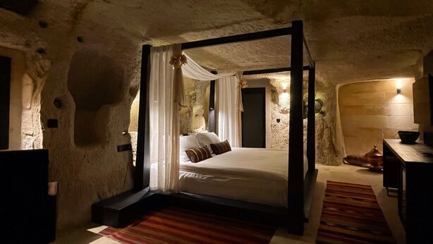 A stone-walled bedroom with a four-poster bed, a wooden bench, and a stone fireplace. - Casa Cappadocia (Ürgüp)