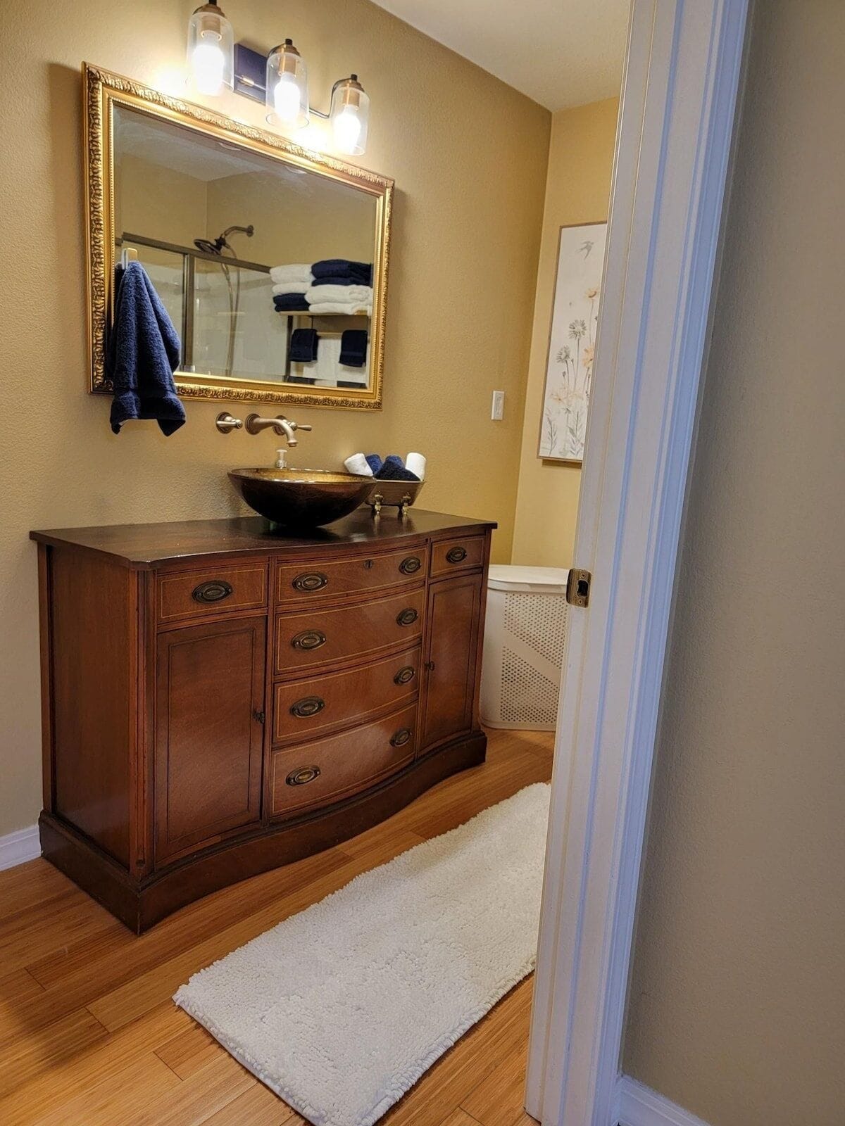A bathroom with a wooden vanity, a large mirror, and a white rug.