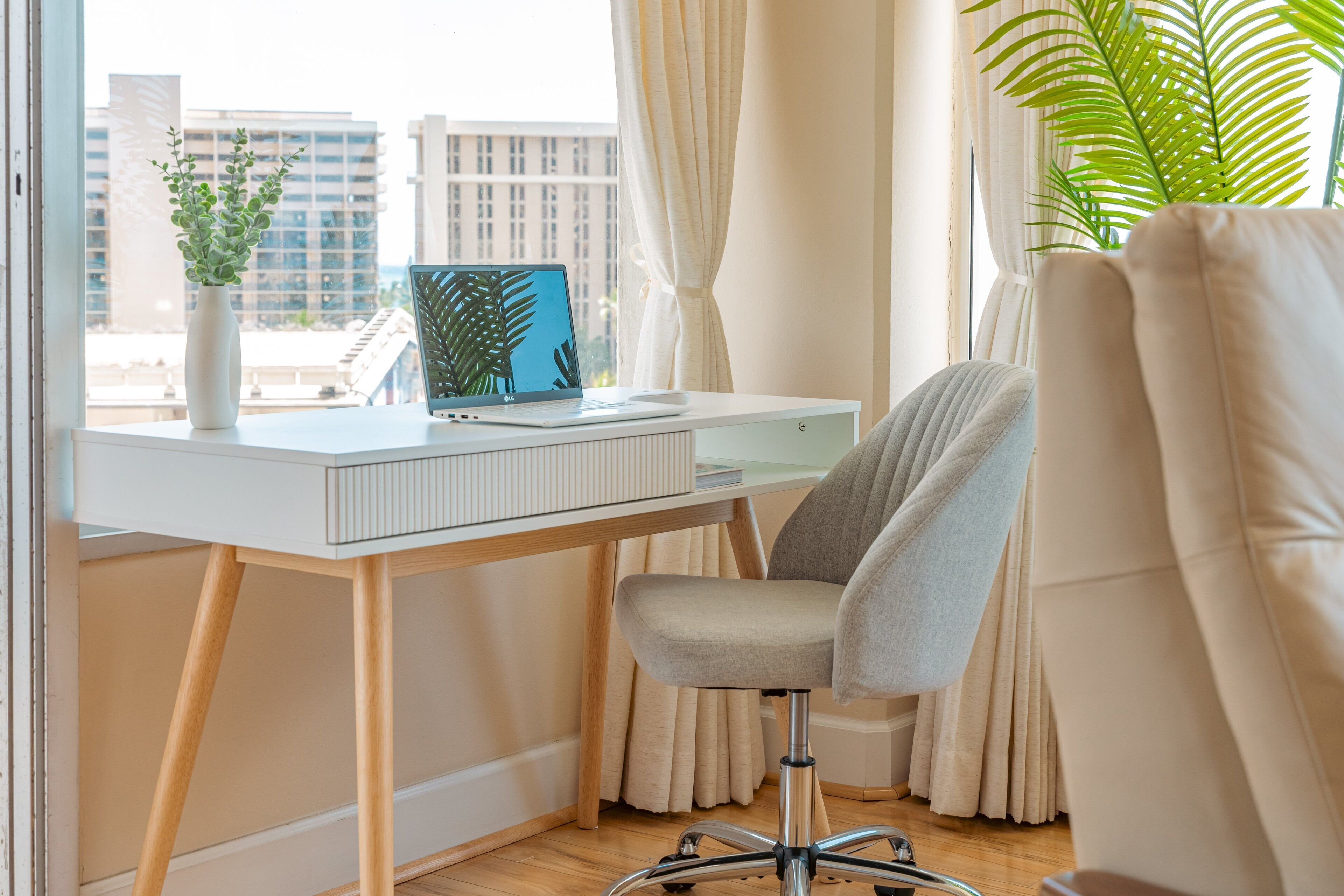A modern office space with a white desk, a grey office chair, a laptop, and a potted plant.