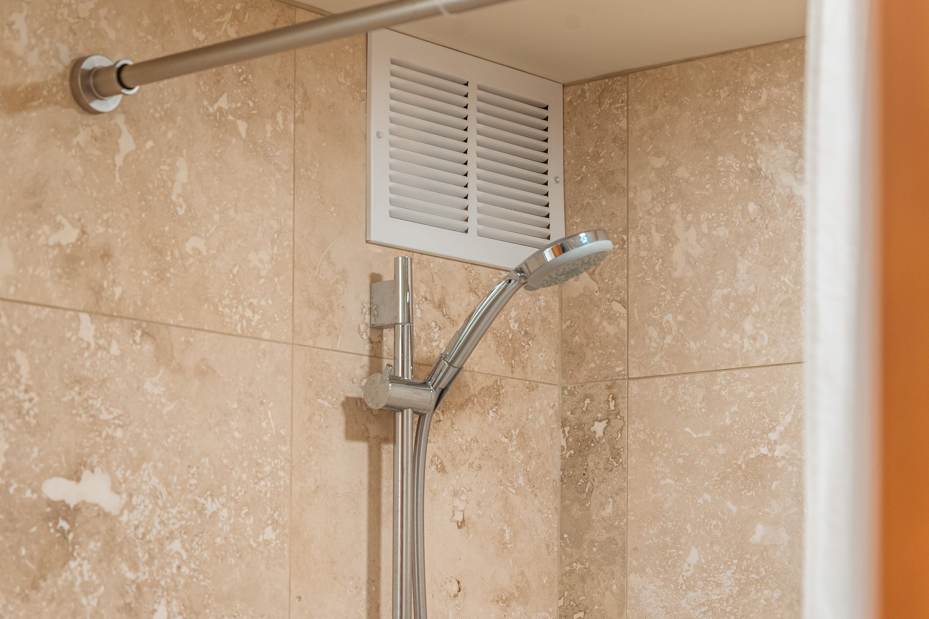 A shower with a handheld showerhead and a wall-mounted control panel.