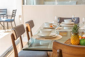 A dining table set with white bowls, plates, and glasses, with a pineapple and fruits on the table. - Ilikai Hotel Condo at Waikiki with Parking (Honolulu)