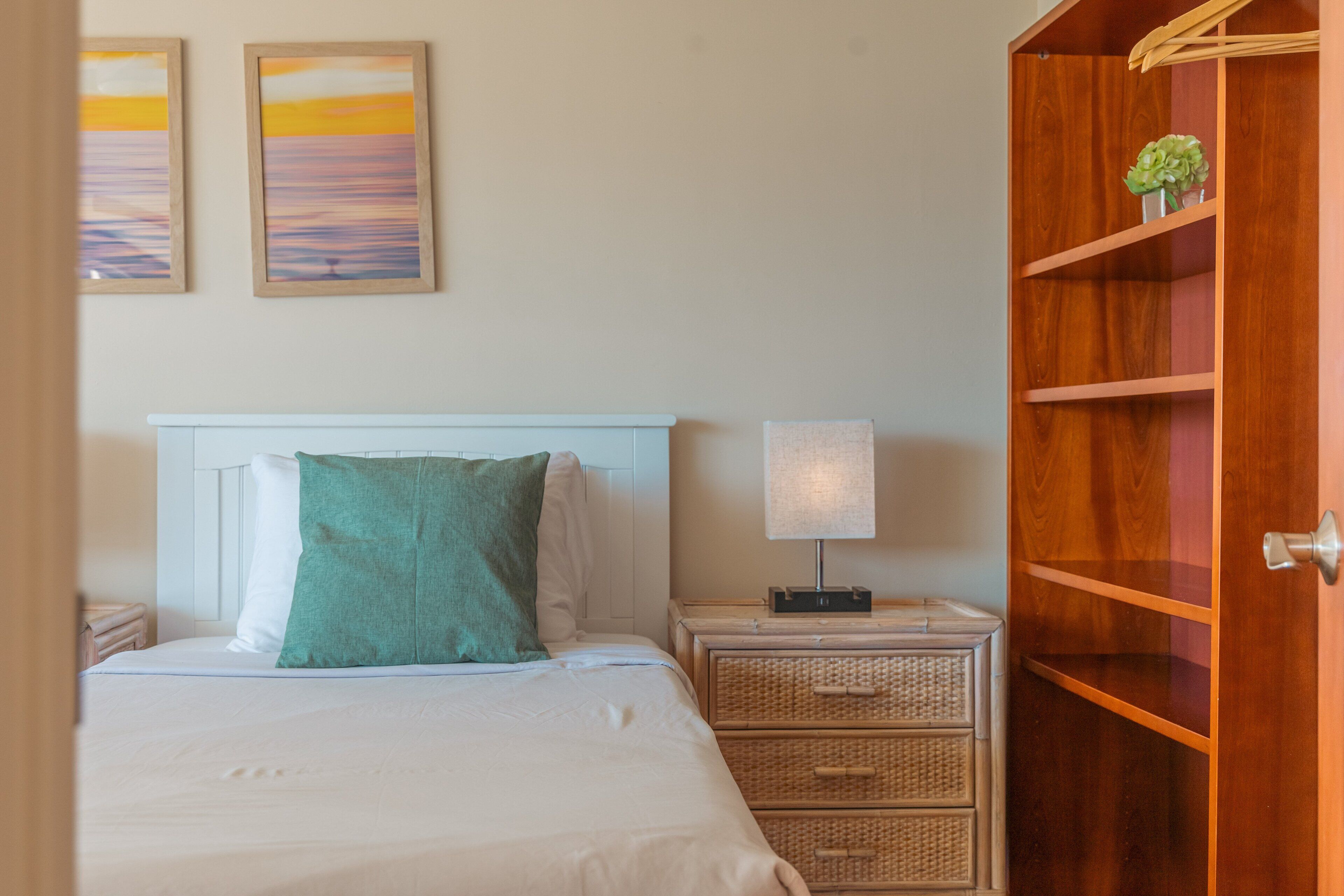 A bedroom with a bed, a nightstand, a lamp, a wooden wardrobe, and two framed pictures on the wall.
