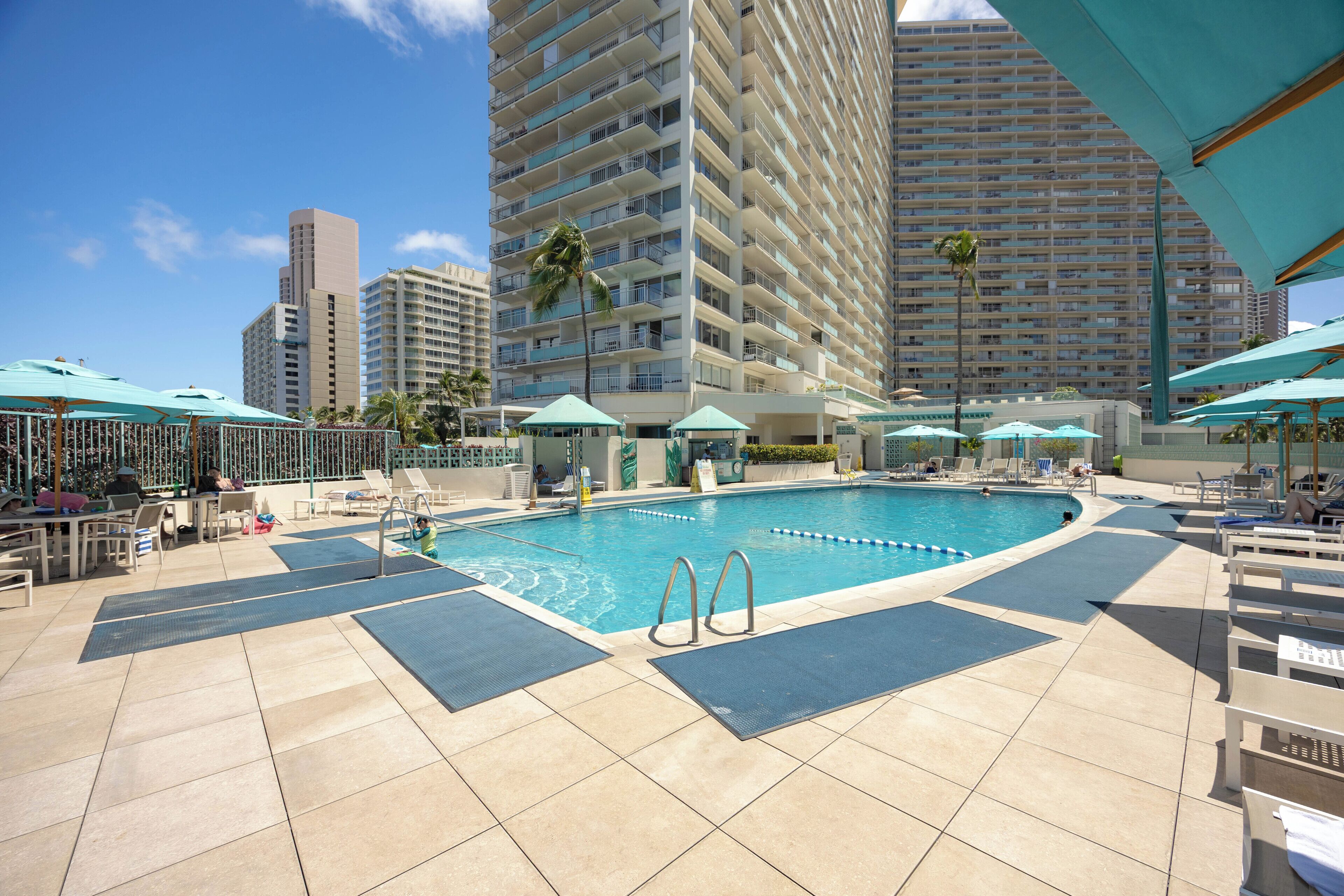 A swimming pool with lounge chairs and umbrellas, surrounded by high-rise buildings.