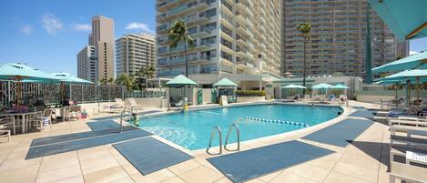 A swimming pool with lounge chairs and umbrellas, surrounded by high-rise buildings.