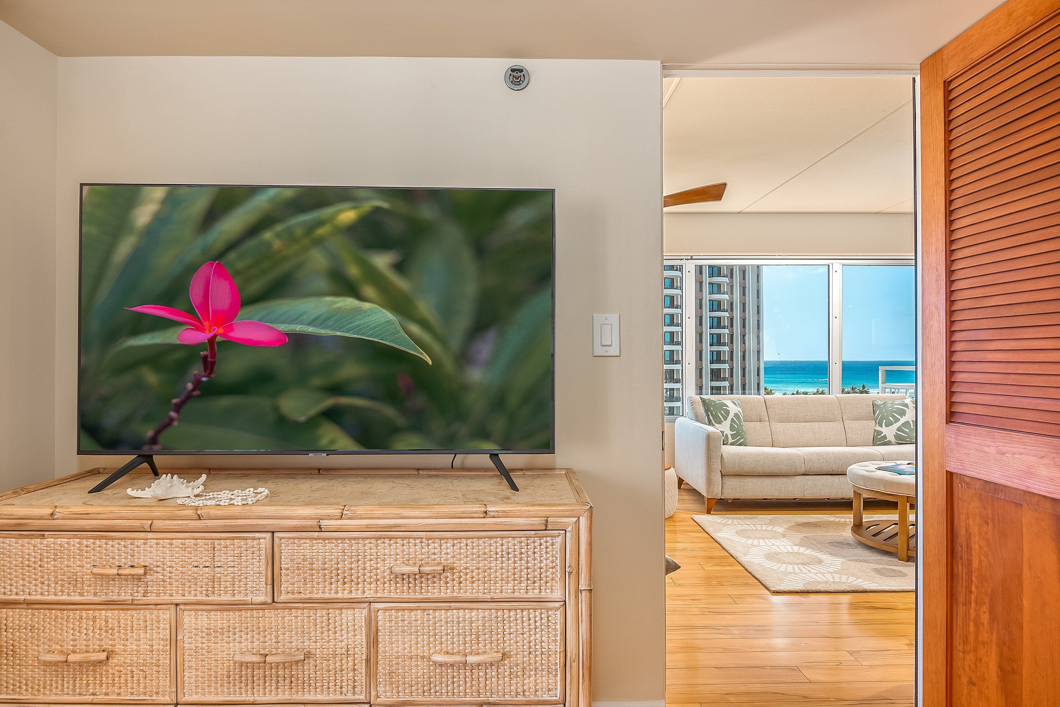 Ein Flachbildfernseher auf einem Rattanmöbelstück, ein Sofa und Meerblick vom Balkon.