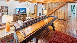 Un salon chaleureux avec une table de billard, une cheminée, un canapé confortable et un escalier menant à un niveau supérieur.