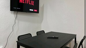 Une pièce avec un téléviseur à  écran plat affichant le logo de Netflix, une table noire et deux chaises noires.