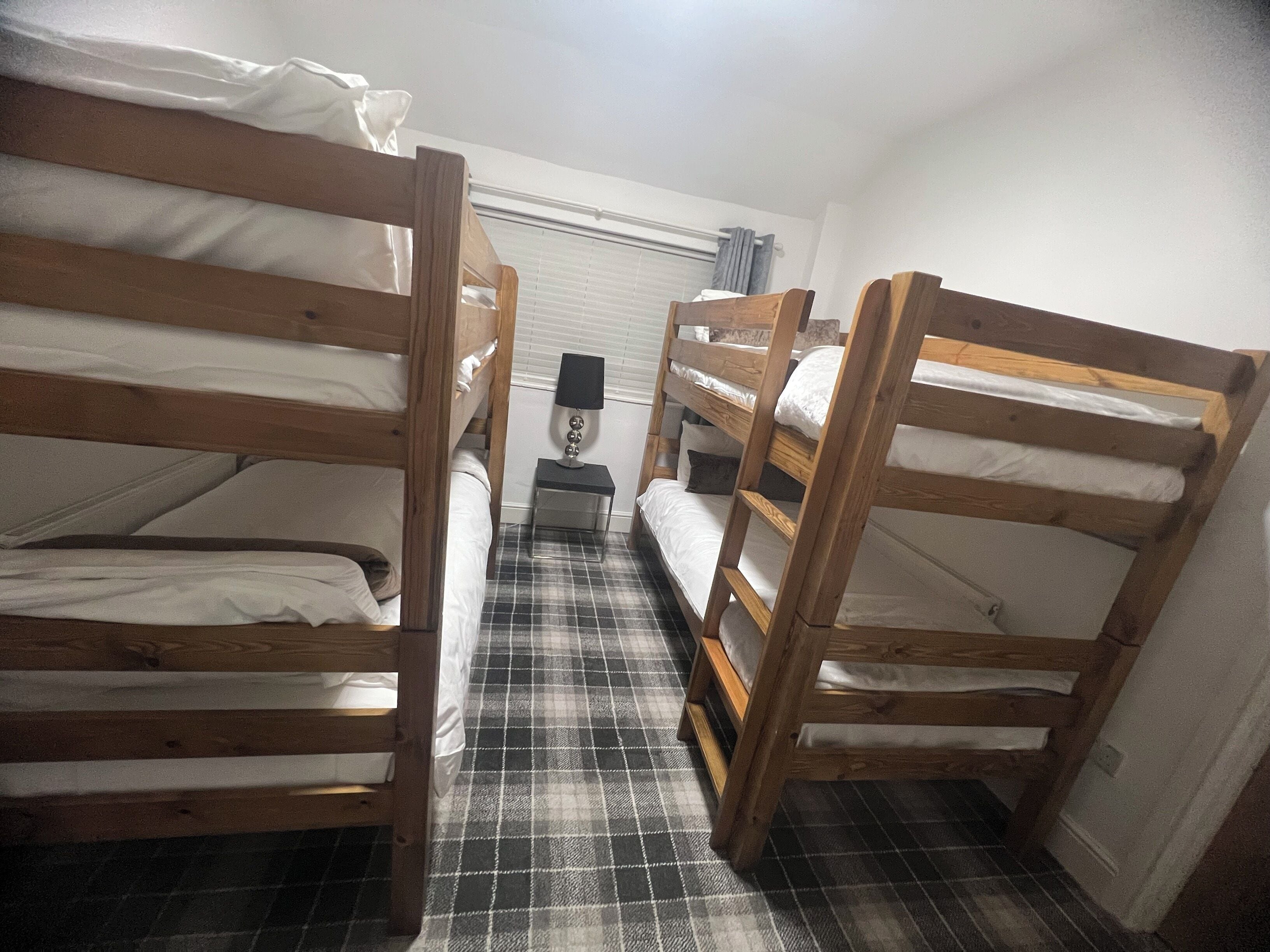 A room with three bunk beds, a small bedside table with a lamp, and a checkered floor.