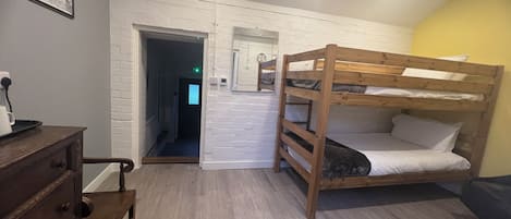A room with a bunk bed, a wooden dresser, a wicker chair, and a white brick wall.