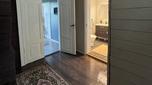 Un corridoio con pavimento in legno, tappeto decorato e porta che conduce a un bagno con il water e il lavandino.