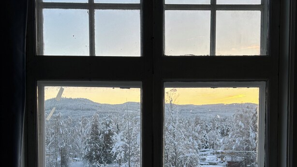 Una finestra con vista su un paesaggio innevato, tra cui alberi e una collina in lontananza.