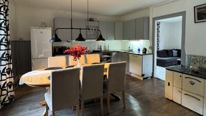 Una cucina moderna con zona pranzo, caratterizzata da un'isola centrale con sedie, illuminazione a sospensione e un vaso con fiori rossi.