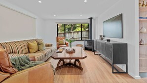 A modern living room with a sofa, a coffee table, a television, and a fireplace. - Ankers Home at Mollymook (Mollymook Beach)