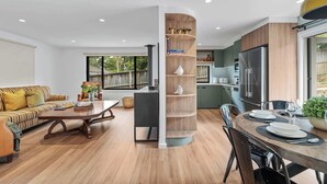 A modern living room with a sofa, coffee table, and a dining area with a table set for four. - Ankers Home at Mollymook (Mollymook Beach)