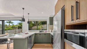 A modern kitchen with a large island, stainless steel appliances, and a view of greenery outside. - Ankers Home at Mollymook (Mollymook Beach)