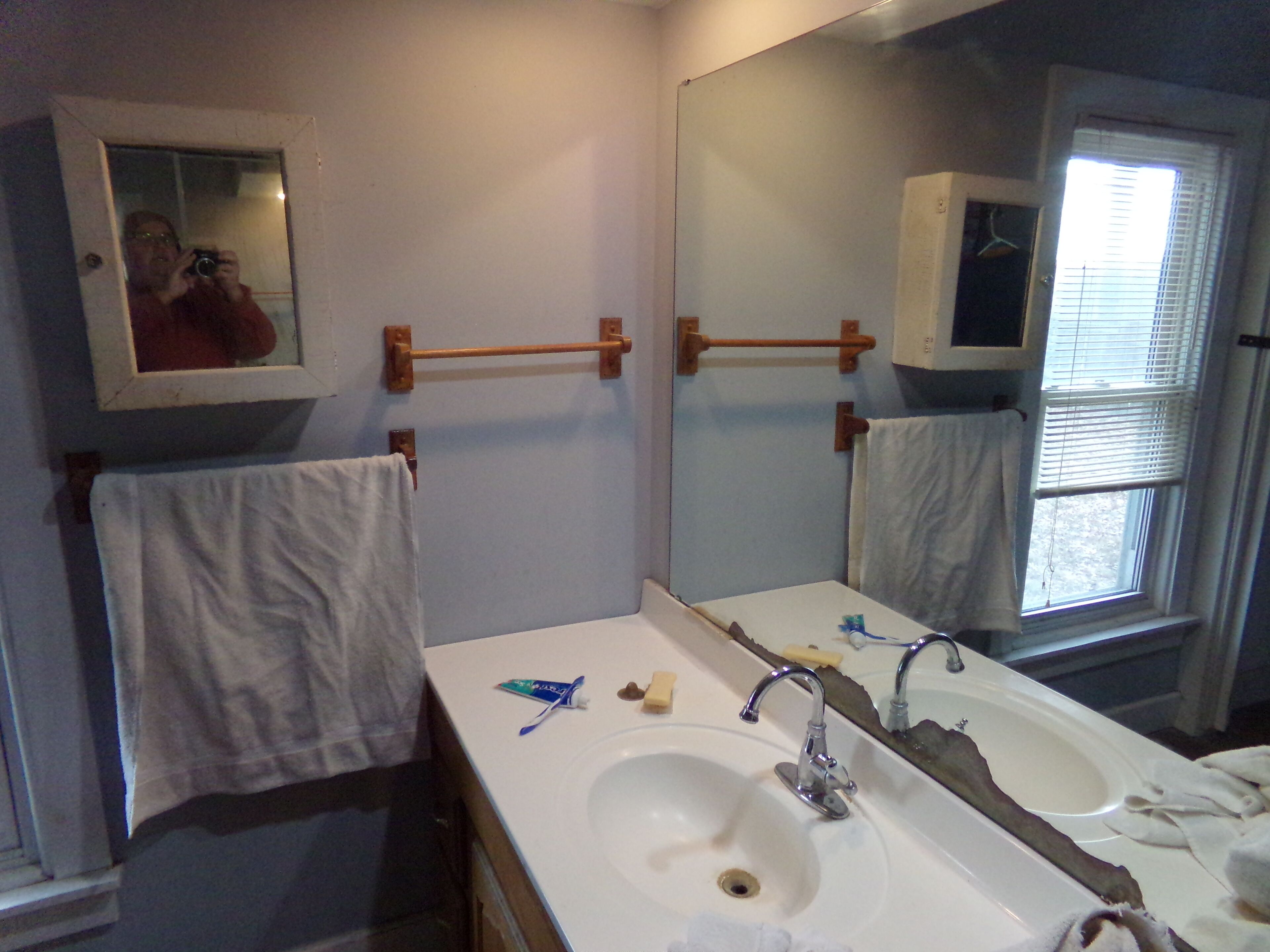 A bathroom with a sink, mirror, towel rack, and window.