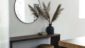 A modern interior with a wooden console table, two round stools, a mirror, and a vase with pampas grass. - Modern 2 bedroom apartment located in a building built in 1896 (Kaslo)
