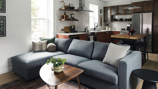 A modern kitchen with a grey sofa, wooden island, and a dining area. - Modern 2 bedroom apartment located in a building built in 1896 (Kaslo)