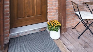 A wooden door with a glass panel, a small potted plant with yellow flowers, and a metal doormat. - Modern 2 bedroom apartment located in a building built in 1896 (Kaslo)