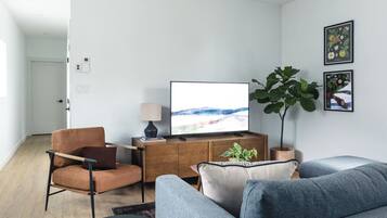 Una sala de estar moderna con un televisor de pantalla plana, un sillón de cuero marrón, un sofá gris y una planta verde grande.