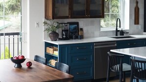 A modern kitchen with dark blue cabinets, a white countertop, and a large window. - Loki’s Loft and Cellar (Kaslo)