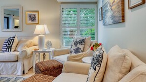 Una sala de estar acogedora con un conjunto de sofás, una mesita de noche con una lámpara y una ventana con persianas.
