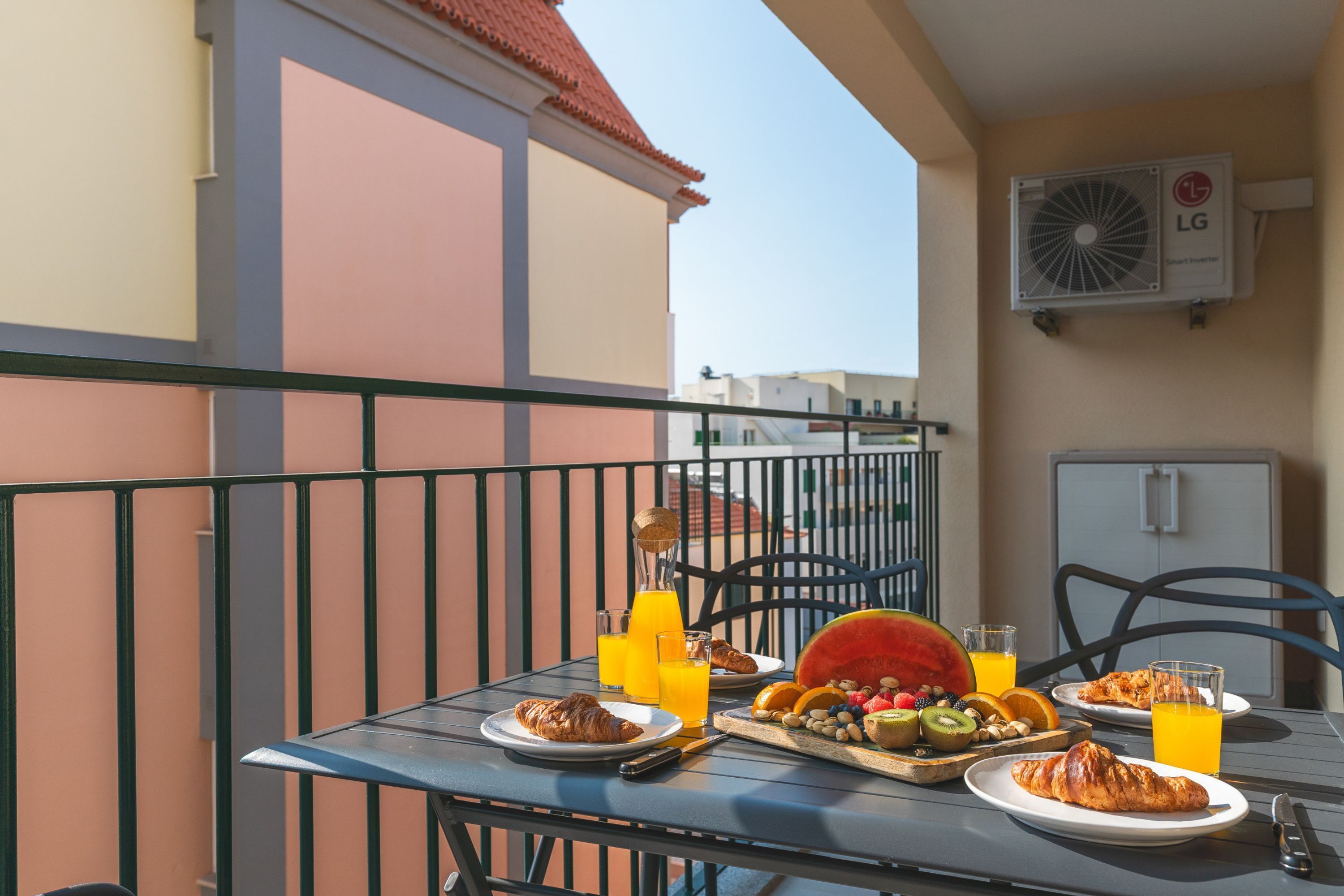 Ein Balkon mit einem Tisch, gedeckt für ein Frühstück, einschließlich Croissants, Obst und Orangensaft.