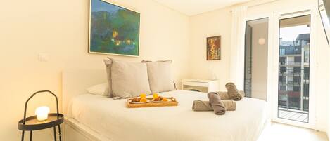 A hotel room with a bed, a bedside table, a chair, a tray with breakfast, and a painting on the wall.