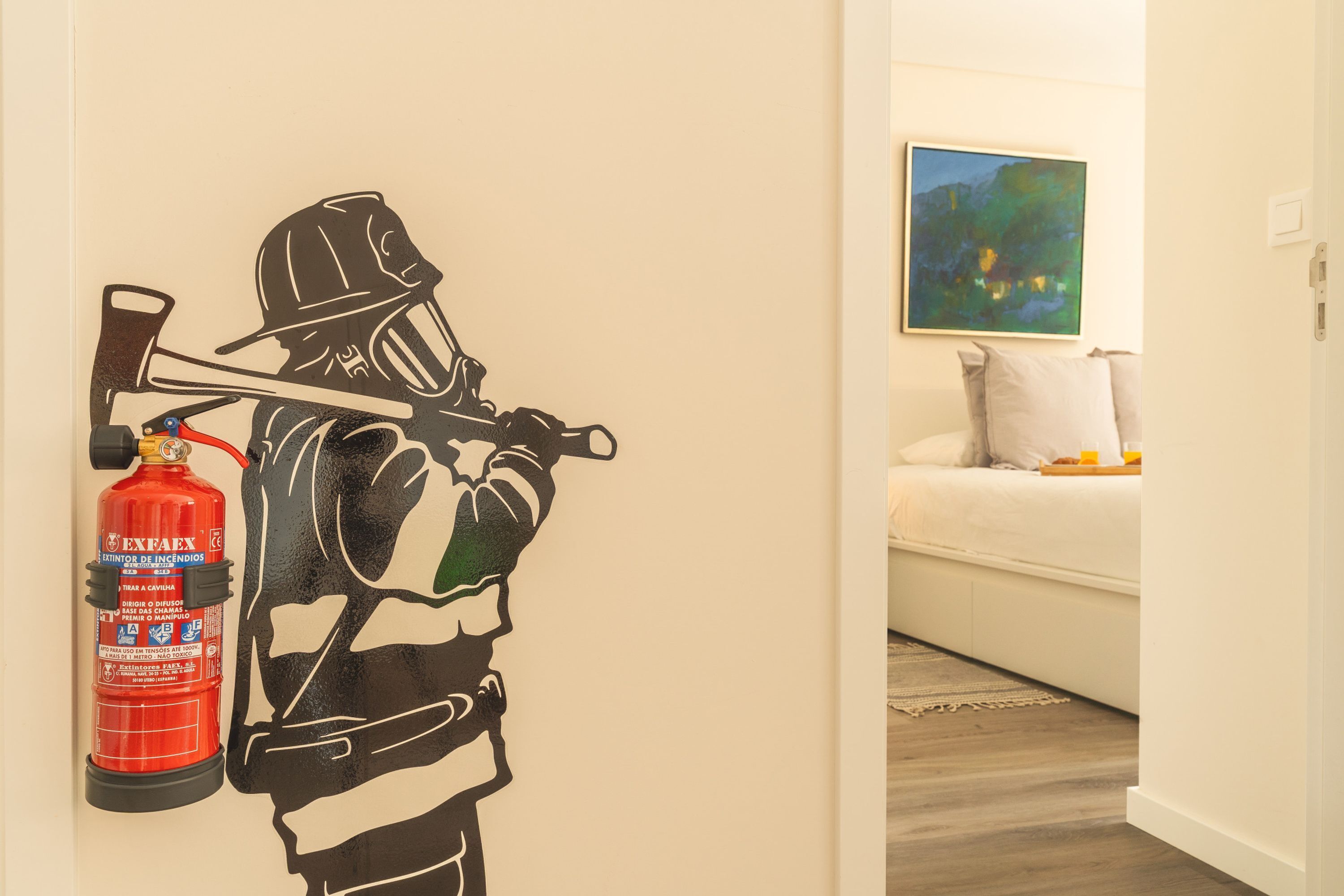 A room with a wall-mounted fire extinguisher and a painting above a white sofa.